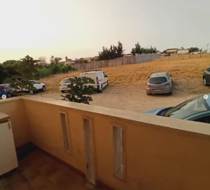 Vue depuis la terrasse d’un appartement en Sicile donnant sur un parking et un terrain.