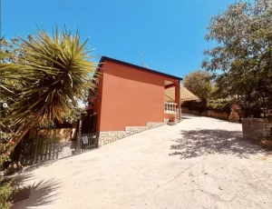 Façade arrière d’une maison rouge en Sicile avec cour spacieuse, ensoleillée et arborée.